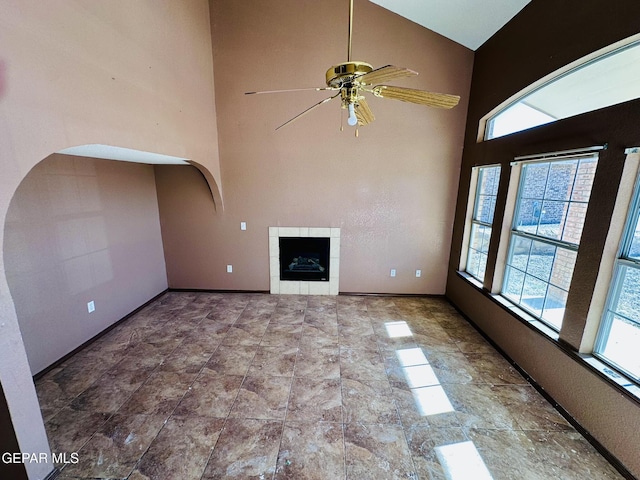 unfurnished living room with ceiling fan, a high ceiling, and a tiled fireplace