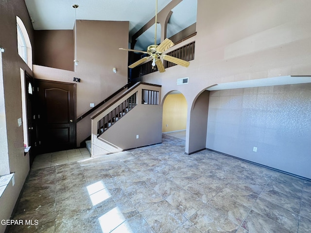 unfurnished living room with ceiling fan, beam ceiling, and high vaulted ceiling