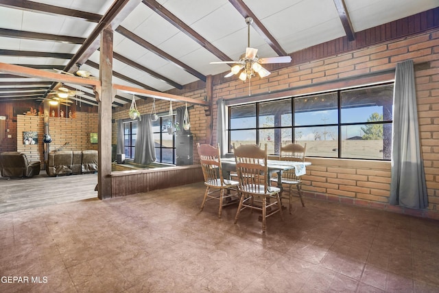 dining space featuring lofted ceiling with beams, a wood stove, ceiling fan, and brick wall