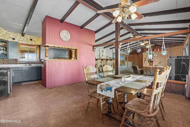 dining space featuring brick wall, ceiling fan, sink, vaulted ceiling with beams, and a stone fireplace