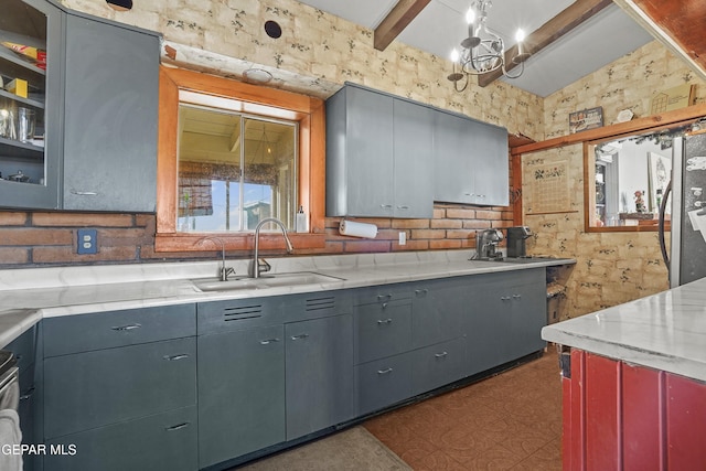 kitchen featuring sink, light stone counters, lofted ceiling with beams, stainless steel fridge, and a chandelier