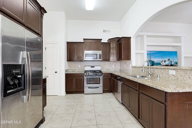 kitchen with light stone counters, dark brown cabinets, stainless steel appliances, sink, and light tile patterned floors