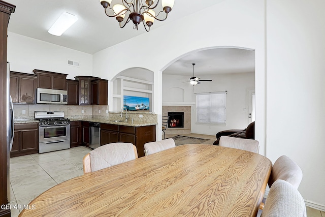 dining space featuring ceiling fan with notable chandelier, light tile patterned flooring, sink, and a tile fireplace