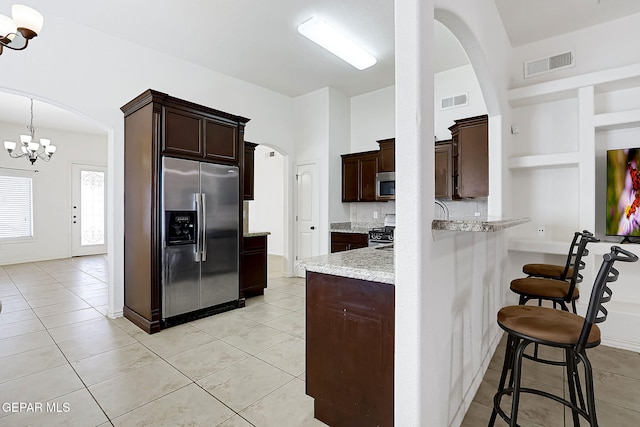 kitchen with an inviting chandelier, light stone counters, pendant lighting, a kitchen bar, and appliances with stainless steel finishes