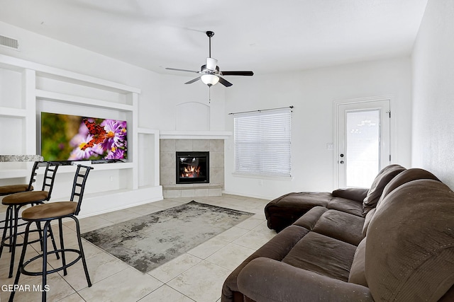 living room featuring a tiled fireplace, ceiling fan, built in features, and light tile patterned floors