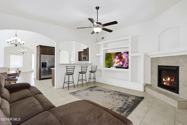 living room with a tile fireplace, light tile patterned floors, ceiling fan with notable chandelier, and lofted ceiling