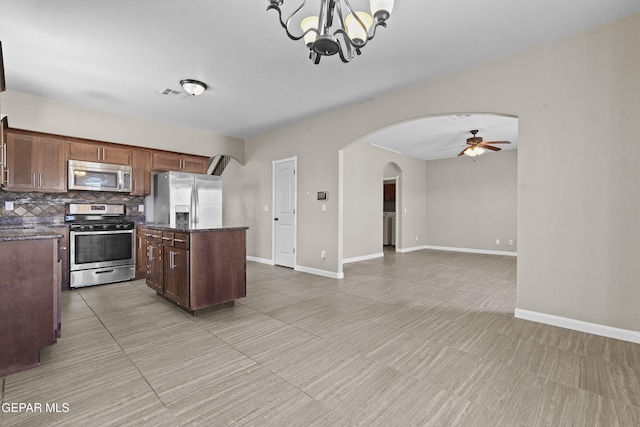 kitchen with decorative backsplash, appliances with stainless steel finishes, ceiling fan with notable chandelier, a kitchen island, and hanging light fixtures