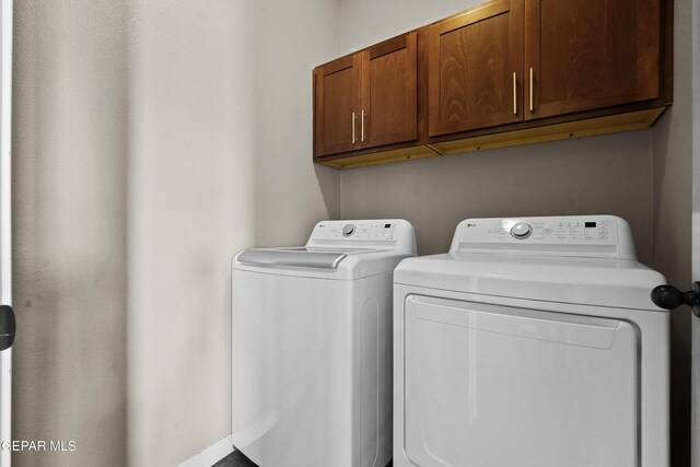 clothes washing area with washer and clothes dryer and cabinets