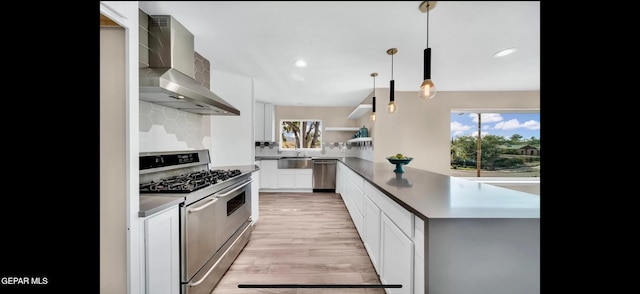 kitchen with wall chimney exhaust hood, light hardwood / wood-style flooring, pendant lighting, white cabinets, and appliances with stainless steel finishes