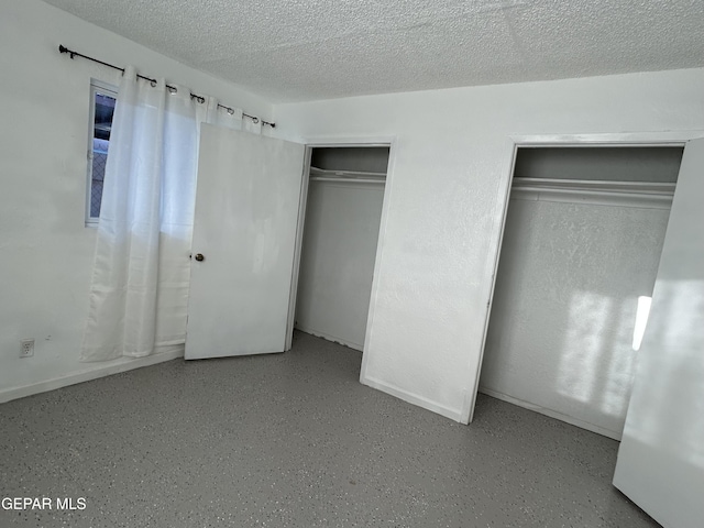 unfurnished bedroom with a textured ceiling and multiple closets