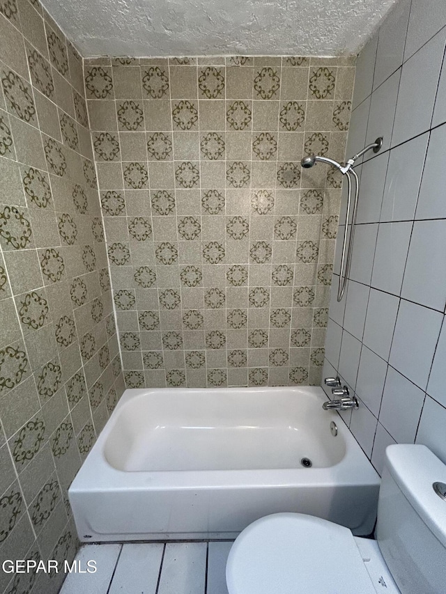 bathroom with toilet, a textured ceiling, tile walls, tiled shower / bath combo, and tile patterned flooring