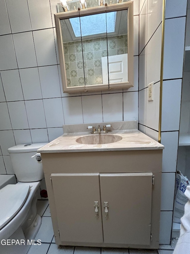 bathroom with toilet, a skylight, tile walls, vanity, and tile patterned flooring