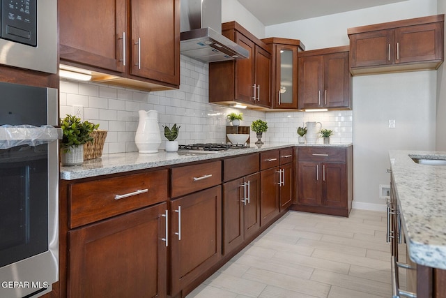 kitchen featuring wall chimney exhaust hood, sink, tasteful backsplash, stainless steel appliances, and light stone countertops