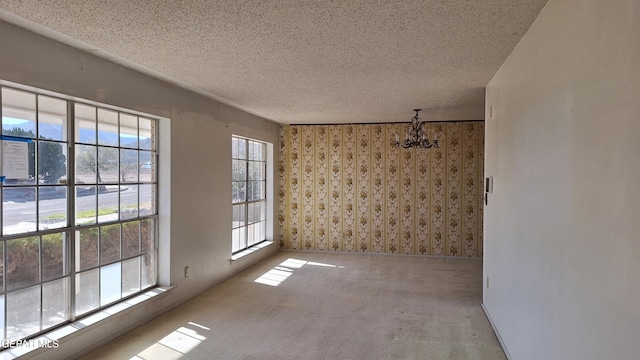 spare room featuring a healthy amount of sunlight, a chandelier, a textured ceiling, and light carpet