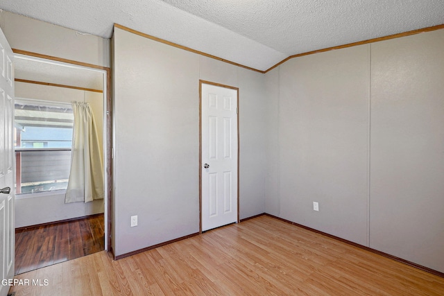 unfurnished bedroom featuring a textured ceiling, crown molding, light hardwood / wood-style flooring, and vaulted ceiling