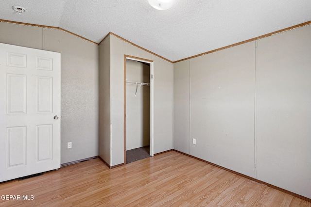 unfurnished bedroom with a textured ceiling, crown molding, light hardwood / wood-style flooring, a closet, and lofted ceiling