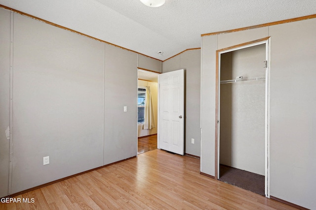 unfurnished bedroom featuring light wood-type flooring, a textured ceiling, crown molding, a closet, and lofted ceiling