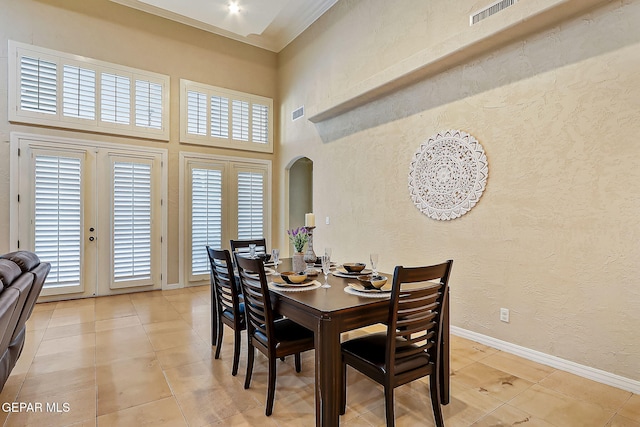 tiled dining room featuring french doors, a towering ceiling, a wealth of natural light, and crown molding