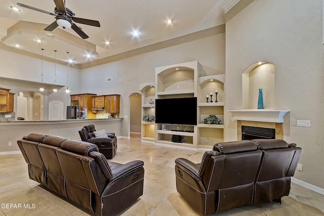 living room with ceiling fan, built in features, a tiled fireplace, a high ceiling, and light tile patterned flooring