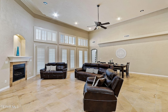 living room featuring ceiling fan, a fireplace, and a towering ceiling