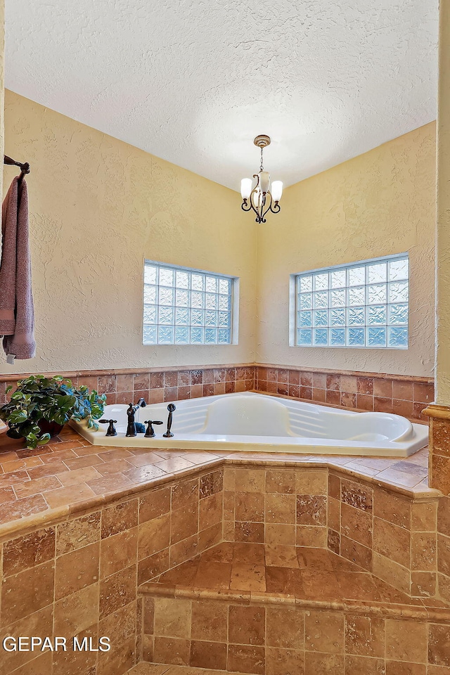 bathroom featuring tiled bath, a wealth of natural light, a textured ceiling, and a notable chandelier