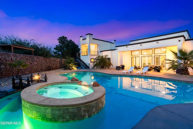 pool at dusk with an in ground hot tub and a patio