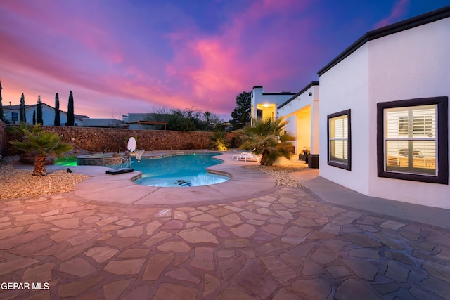 pool at dusk featuring a patio area and an in ground hot tub