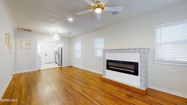 unfurnished living room featuring ceiling fan with notable chandelier and wood-type flooring