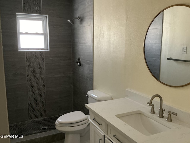 bathroom featuring toilet, a tile shower, and vanity