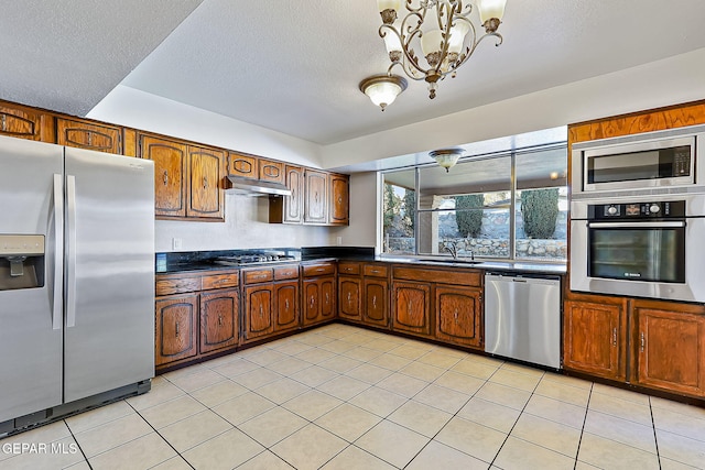 kitchen featuring a textured ceiling, stainless steel appliances, sink, light tile patterned floors, and an inviting chandelier