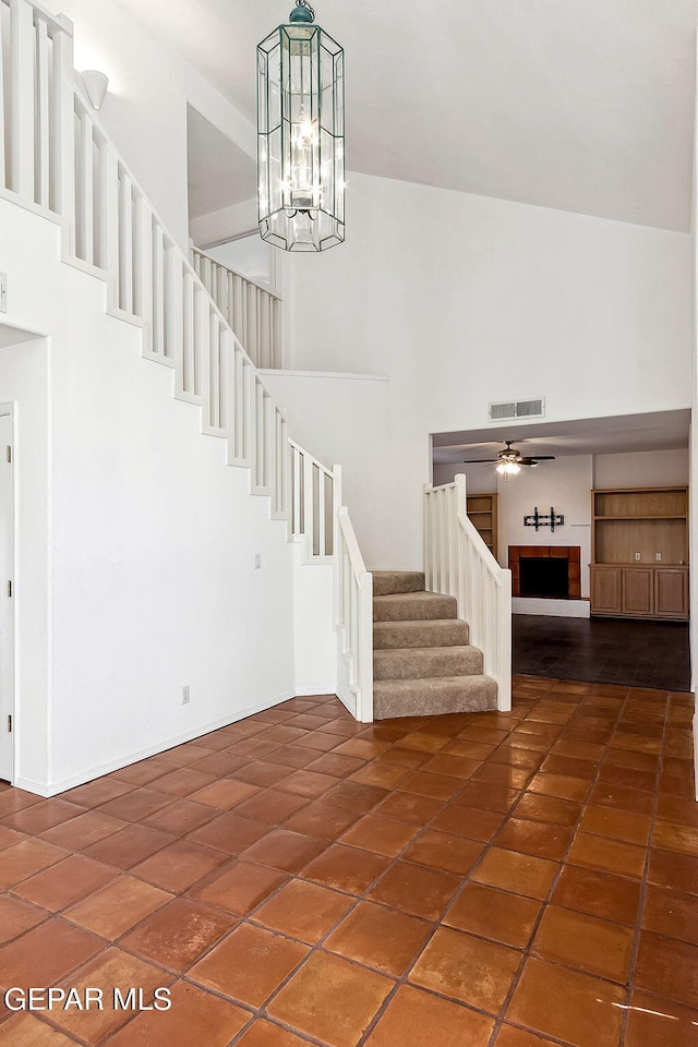 stairs with tile patterned flooring, a high ceiling, and ceiling fan with notable chandelier