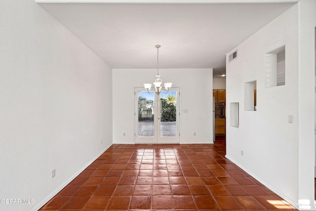 unfurnished dining area with dark tile patterned flooring, an inviting chandelier, and french doors