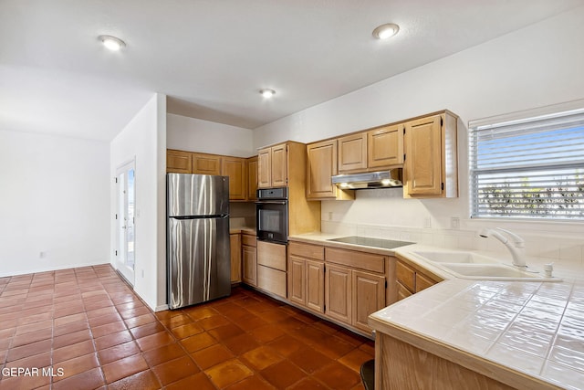 kitchen with sink, tile countertops, light brown cabinetry, black appliances, and dark tile patterned flooring