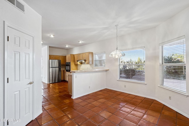 kitchen with kitchen peninsula, light brown cabinetry, oven, hanging light fixtures, and stainless steel refrigerator