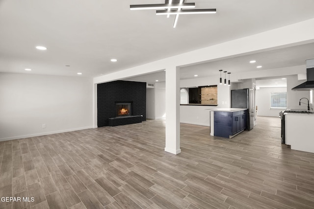 unfurnished living room with light wood finished floors, a fireplace, a sink, and recessed lighting