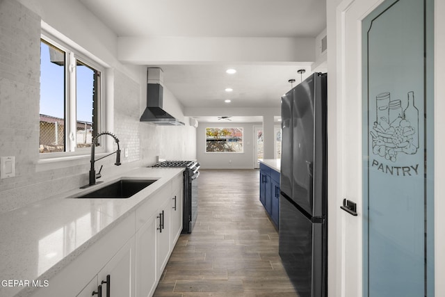 kitchen with freestanding refrigerator, gas stove, a sink, wood finished floors, and wall chimney exhaust hood