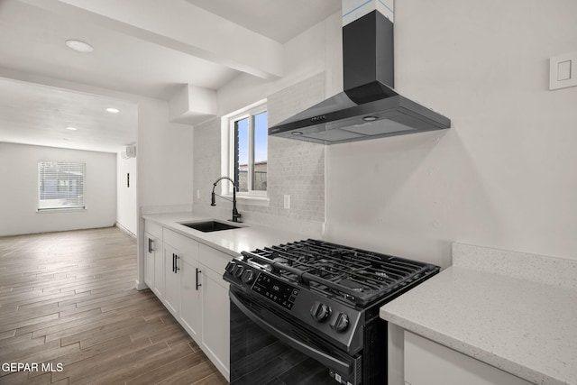 kitchen featuring decorative backsplash, a sink, black gas stove, wall chimney range hood, and wood finished floors