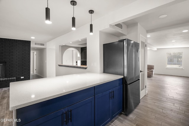 kitchen featuring a fireplace, light wood finished floors, blue cabinetry, visible vents, and freestanding refrigerator