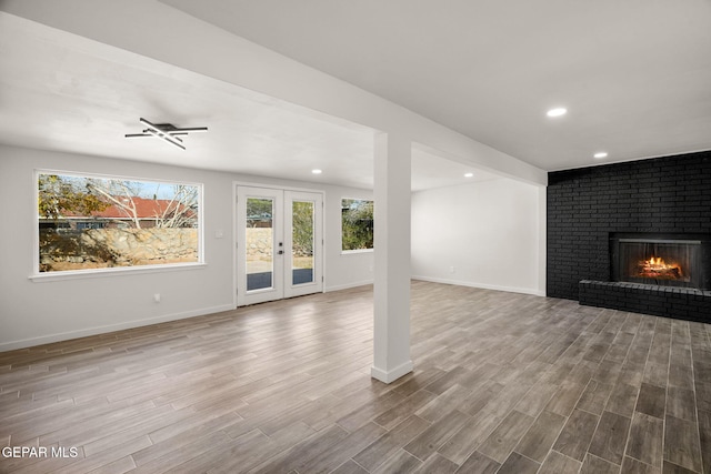 unfurnished living room featuring recessed lighting, a fireplace, wood finished floors, baseboards, and french doors