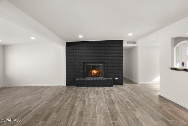 unfurnished living room with baseboards, visible vents, wood finished floors, a fireplace, and recessed lighting