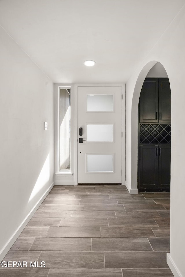 foyer entrance with arched walkways, wood finish floors, and baseboards