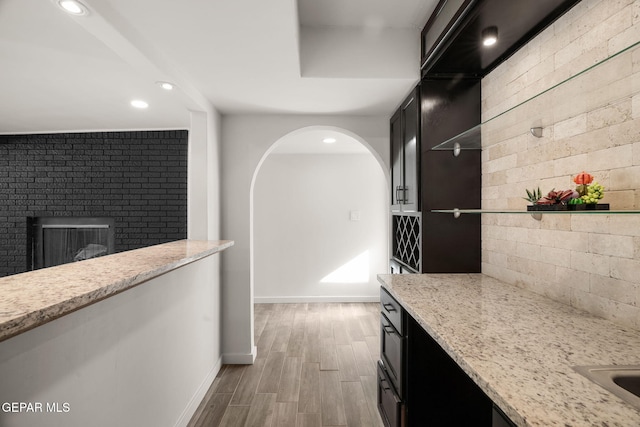 kitchen featuring light stone countertops, dark cabinets, wood finished floors, and recessed lighting