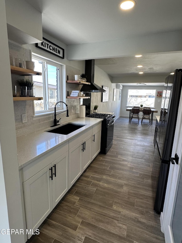 kitchen with dark wood-style floors, open shelves, a sink, wall chimney range hood, and black appliances