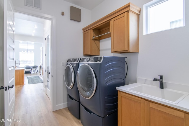 clothes washing area with cabinets, sink, light wood-type flooring, a notable chandelier, and washing machine and clothes dryer