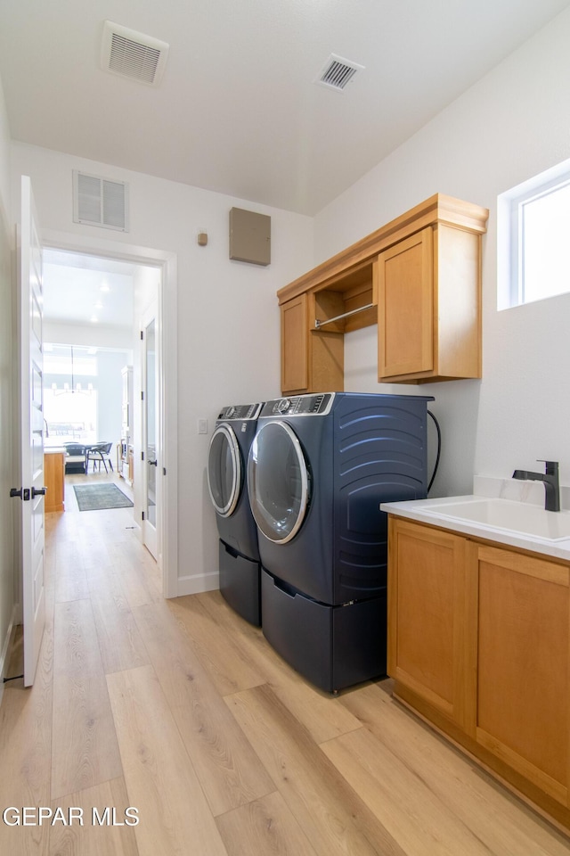 laundry room featuring cabinets, a healthy amount of sunlight, sink, washing machine and clothes dryer, and light hardwood / wood-style floors