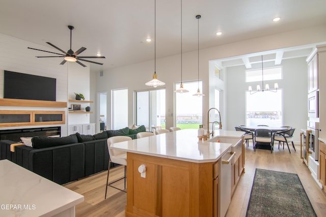 kitchen with built in microwave, a center island with sink, ceiling fan with notable chandelier, and light wood-type flooring