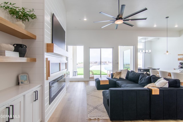 living room featuring a large fireplace, ceiling fan with notable chandelier, and light wood-type flooring