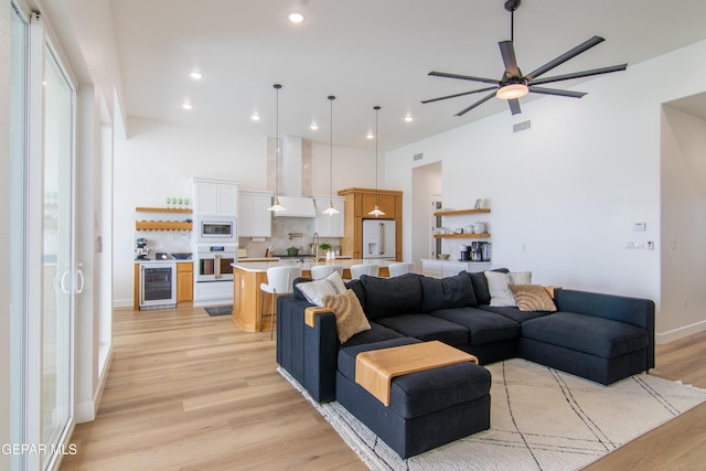 living room with ceiling fan, light wood-type flooring, and beverage cooler