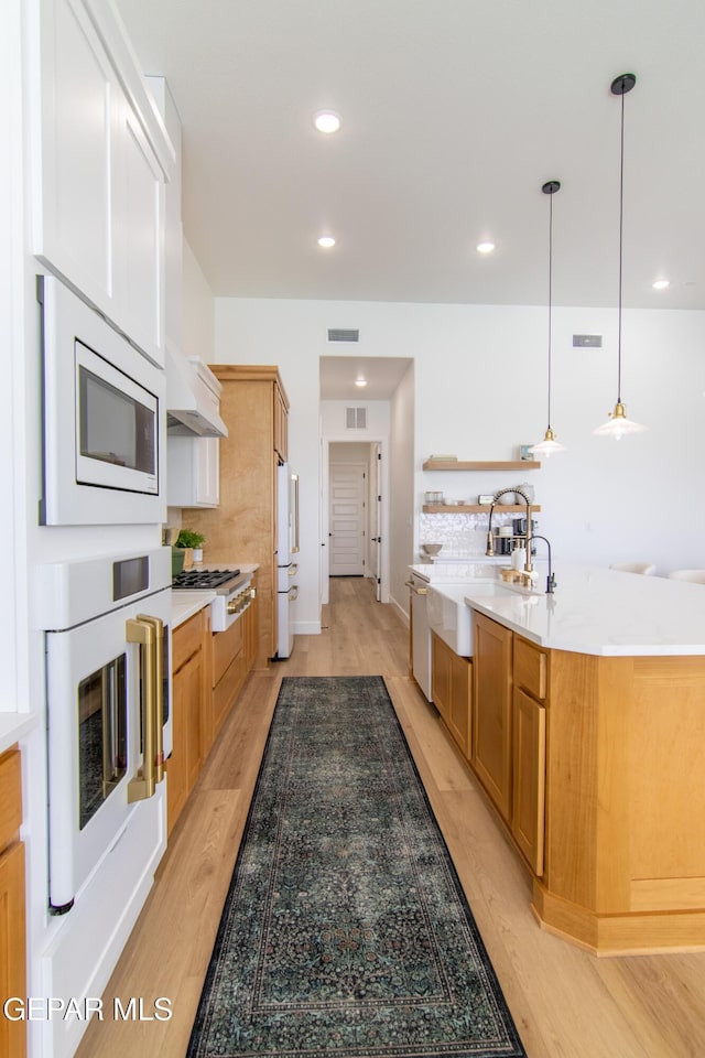 kitchen with decorative backsplash, appliances with stainless steel finishes, sink, decorative light fixtures, and light hardwood / wood-style flooring