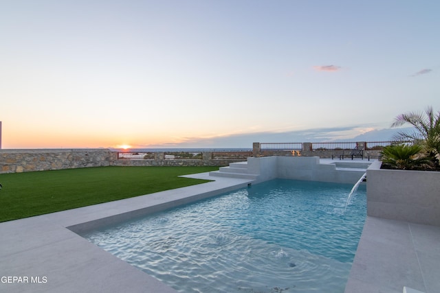 pool at dusk with pool water feature and a lawn